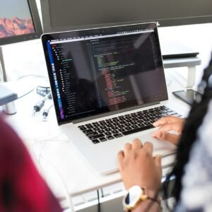 A woman coding on a laptop in a modern office environment with multiple monitors.